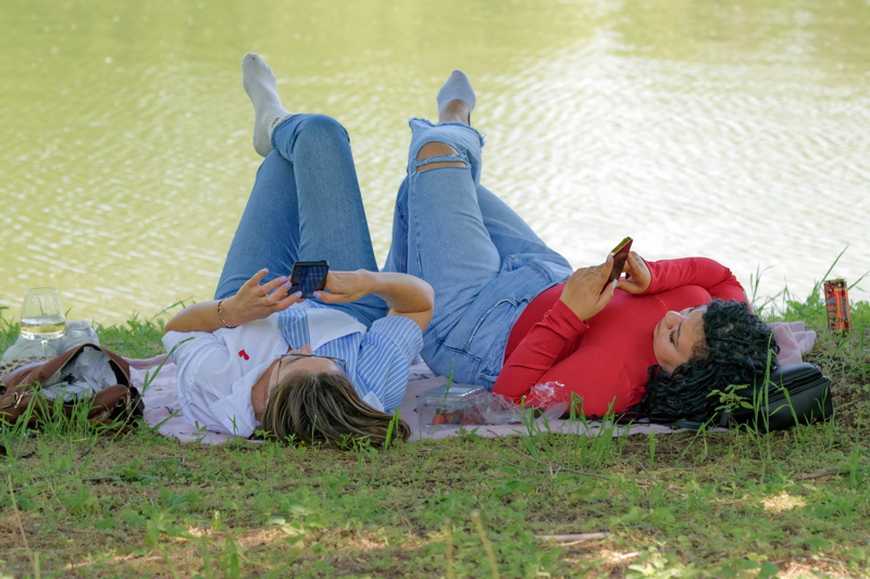 Girls with smartphones lying on lakeshore